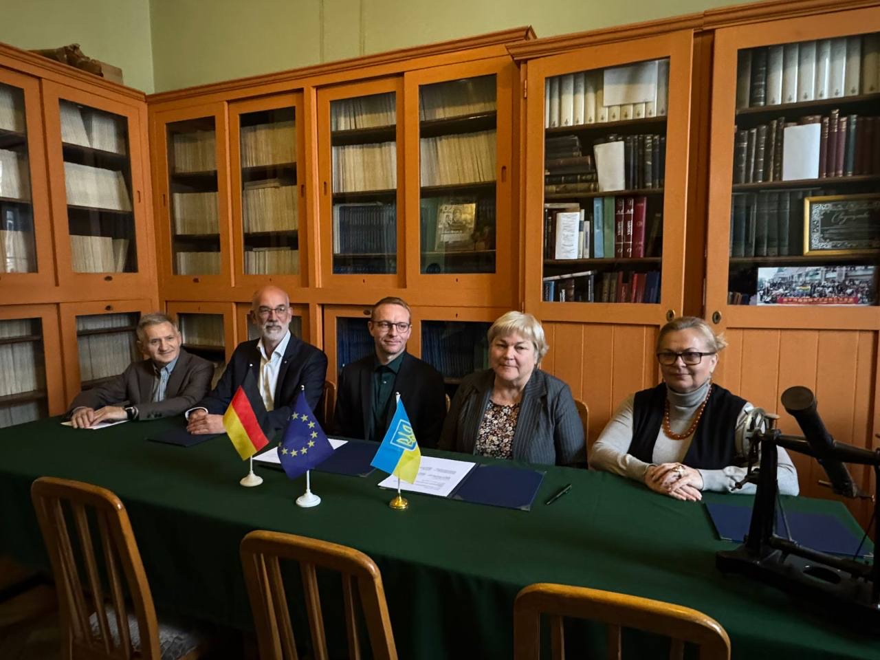 Five representatives seated at a table with German, European Union and Ukrainian flags during the signing of the letter of intent in Lviv.