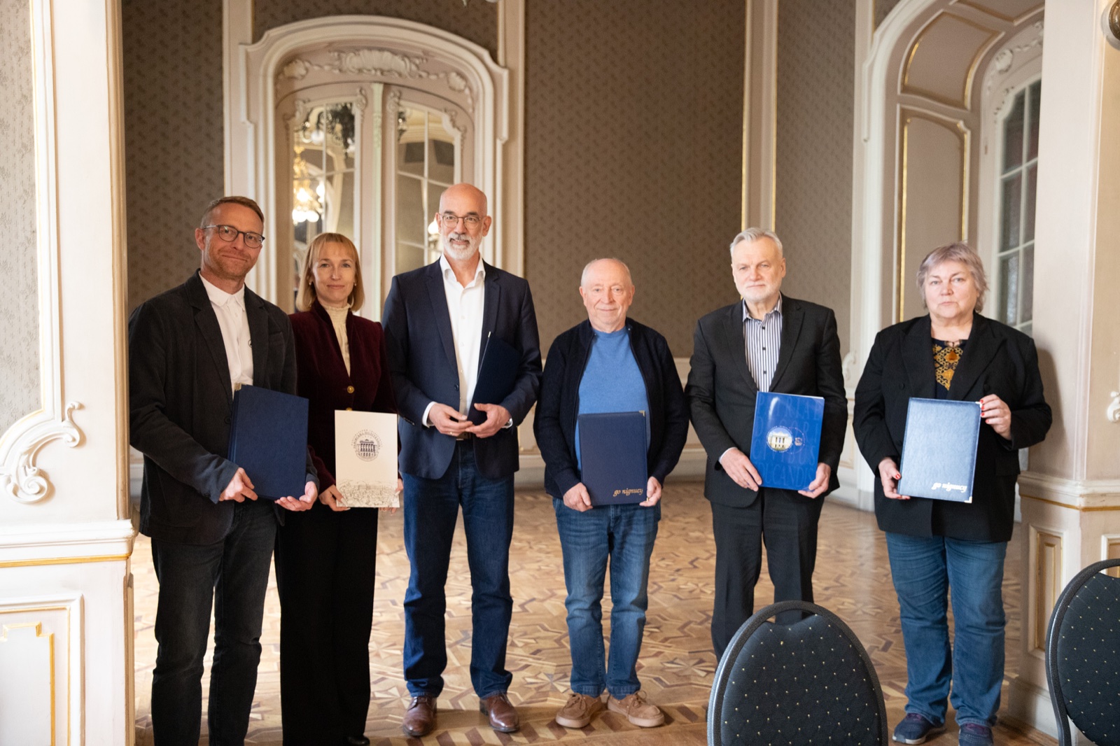 Six signatories standing side by side holding the signed memorandum folders in a historic hall in Lviv.