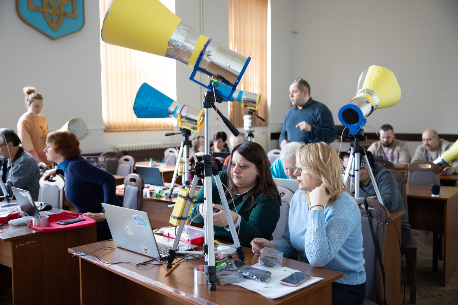 Teachers in a classroom assembling self-made horn radio telescopes in blue and yellow, with laptops on the desks.