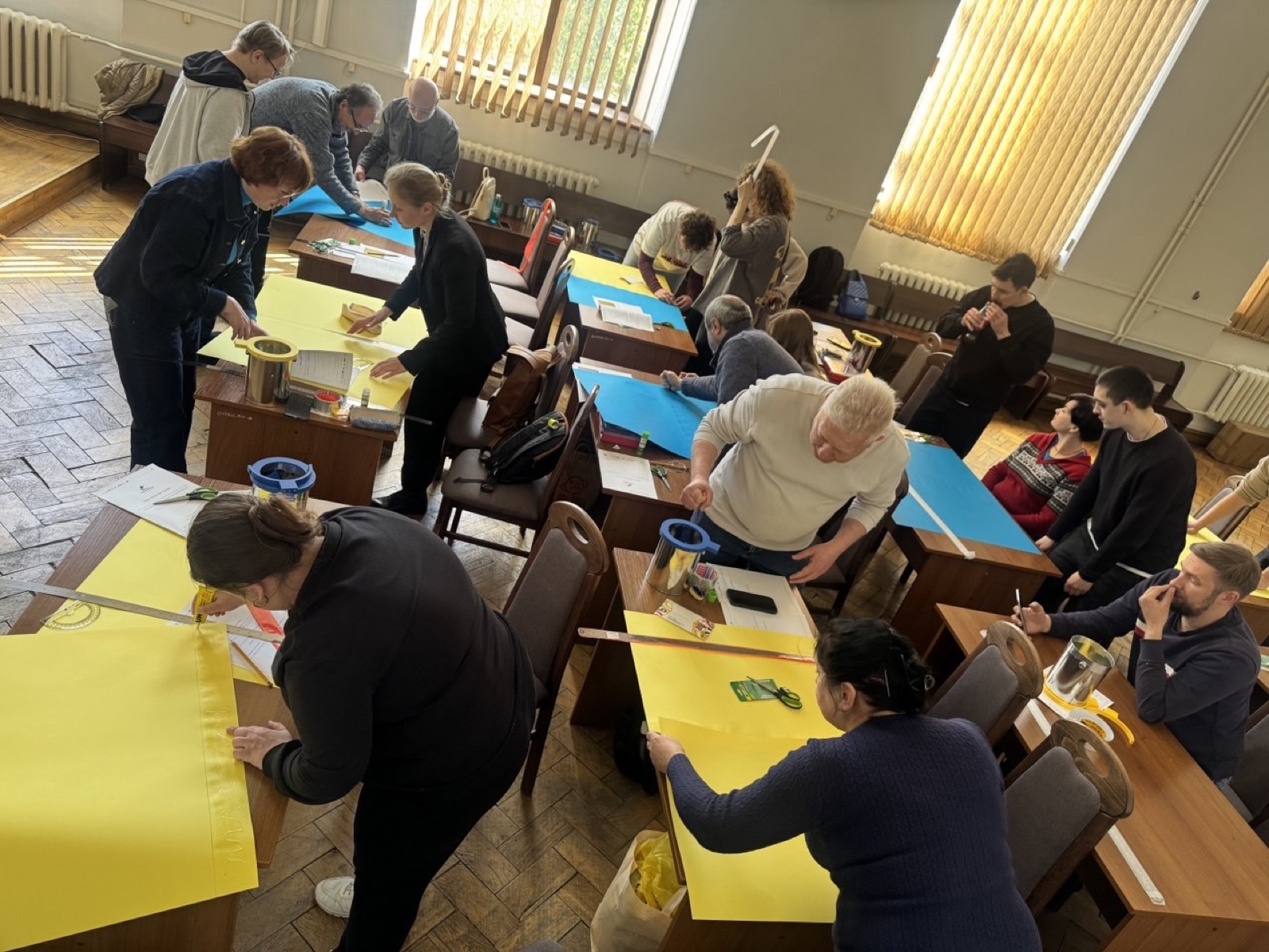 Participants around classroom tables cutting and folding yellow and blue sheets into horn antennas.