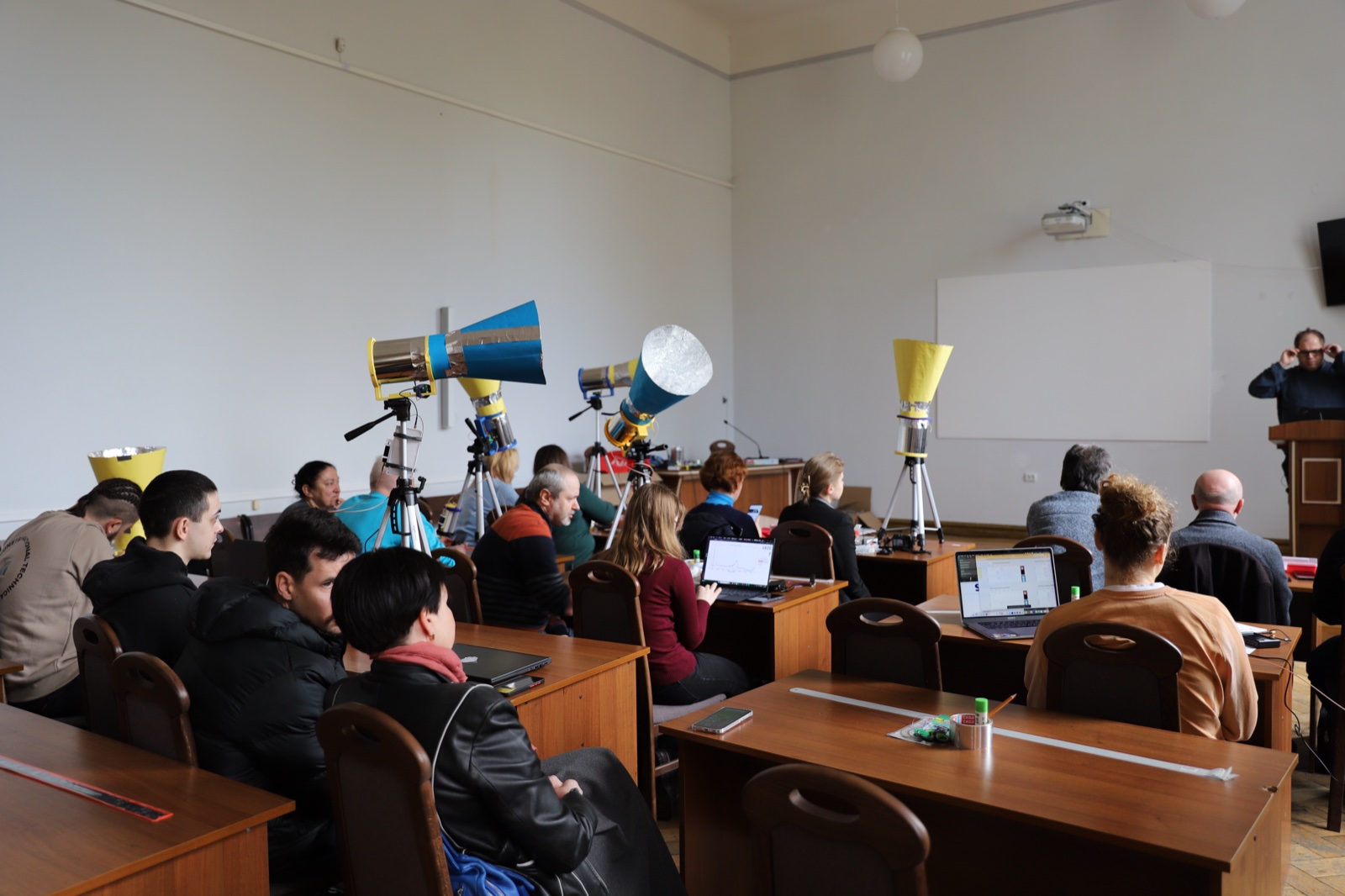 Workshop room with several assembled horn telescopes on tripods and participants working on laptops.