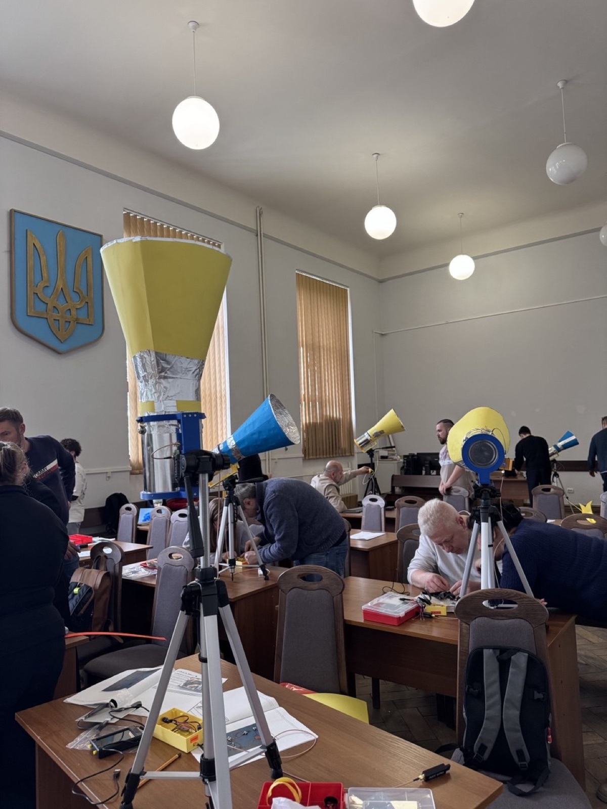 Finished blue and yellow horn radio telescopes on tripods in a hall with the Ukrainian trident on the wall.